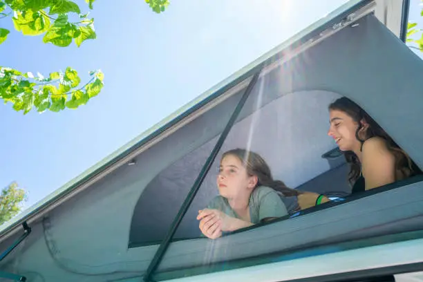 Sister teen girls at camper van window relaxed