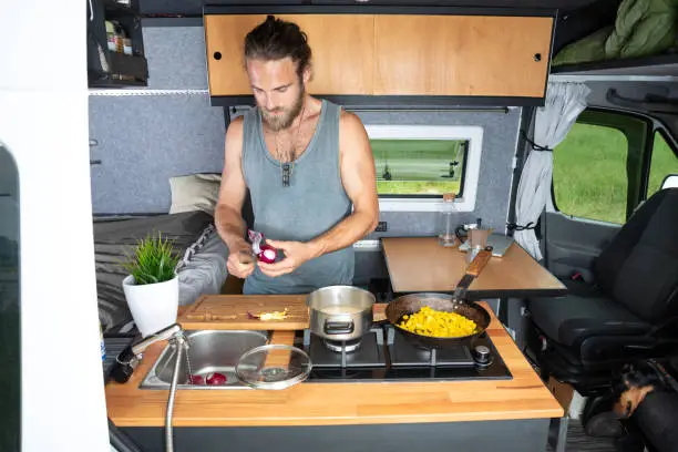 A young bearded man is cooking inside his self build camper van.