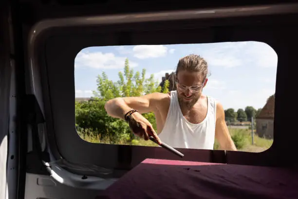 Interior view of a van. A man is refining the edge of a hole he cut in order to install a window.