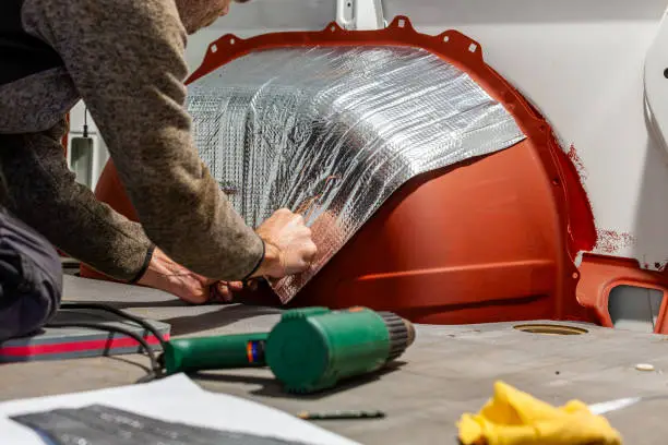 DIY Camper Jumper van conversion. aluminium butyl mats. using man using hot air gun. Adhesive Noise Insulation Mat inside motorhome. Car, foam insulation effect, sound absorption. Noise Protection
